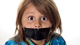 A little boy with long hair and duct tape over his mouth and a surprised expression. | Andi Berger | Dreamstime.com