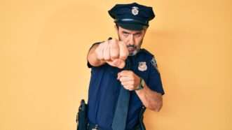 A policeman against an orange background, punching with his fist toward the camera. | Aaron Amat | Dreamstime.com