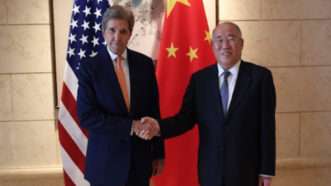 John Kerry shakes hands with PRC Special Envoy for Climate Change Xie Zhenhua in front of flags for the United States and China | State Department