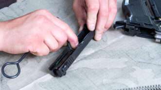 A man cleans the receiver of a disassembled handgun. | DPST/Newscom