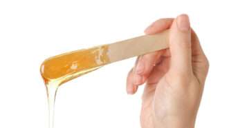 A hand holds a wooden stick with sugaring paste | Photo 115683249 © Chernetskaya | Dreamstime.com