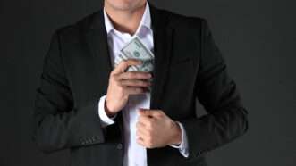 A man tucks a wad of cash into a suit jacket pocket. | Chernetskaya | Dreamstime.com