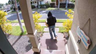 A package thief in a hoodie walks away from a porch with a package in tow, as seen through a doorbell camera. | RightFramePhotoVideo | Dreamstime.com
