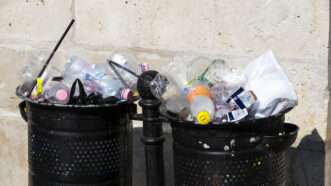 Two street trash cans filled to the top with garbage and plastic bottles. | Lestertairpolling | Dreamstime.com