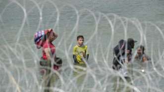 Migrants wading through water near a razor wire barrier | Bob Daemmrich/ZUMAPRESS/Newscom