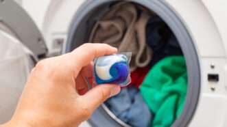 Close-up of a person's hand as they are about to put a laundry pod into a full washing machine. | Ocskay Mark | Dreamstime.com