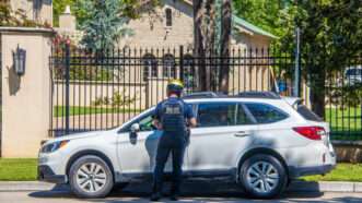 A police officer stands next to a crossover SUV that has been pulled over in front of a gated residential home. | Susan Vineyard | Dreamstime.com