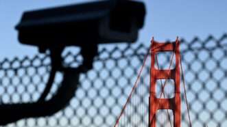 A surveillance camera in the foreground with the Golden Gate Bridge visible in the background, separated by a chain link fence. | Bumbleedee | Dreamstime.com