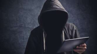 An anonymous man in a hoodie browses the internet on a tablet. | Stevanovicigor | Dreamstime.com