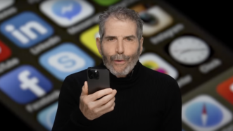 John Stossel holds a cellphone in front of an enlarged smart phone screen | Stossel TV