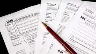 IRS tax forms against a black background, with a ballpoint pen sitting on top. | James Martin | Dreamstime.com