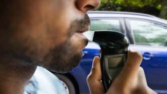 A male motorist blows into a Breathalyzer while sitting in the front seat of his car. | Andrey Popov | Dreamstime.com