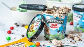 A pint of Ben & Jerry's "half baked" ice cream, with the lid leaning against it and an ice cream scoop laying on top. An open bag of M&Ms is also on the table. | Photo by <a href="https://unsplash.com/@hybridstorytellers?utm_content=creditCopyText&utm_medium=referral&utm_source=unsplash">Hybrid Storytellers</a> on <a href="https://unsplash.com/photos/ben-and-jerrys-chocolate-fudge-brownie-ice-cream-pugrrx5NtAA?utm_content=creditCopyText&utm_medium=referral&utm_source=unsplash">Unsplash</a>