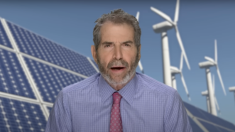 John Stossel stands in front of solar panels and wind turbines | Stossel TV