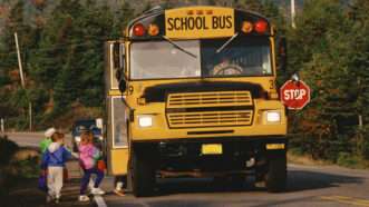 Children board a yellow school bus idling on a two-lane road. | Joe Sohm | Dreamstime.com
