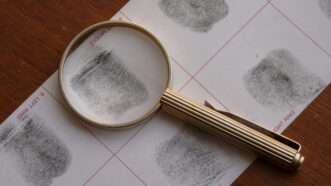 Magnifying glass sits atop a card of fingerprints. | Drzaribu | Dreamstime.com