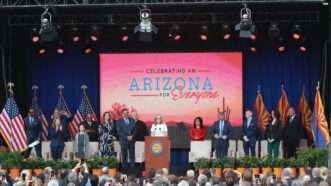 Elected officials in Arizona stand on a stage in front of a screen that reads, "Celebrating an Arizona for Everyone." | Alexandra Buxbaum/Sipa USA/Newscom