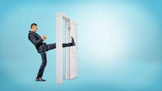 A man in a business suit kicks open the door of a solitary door frame against a light blue background. | Gearstd | Dreamstime.com