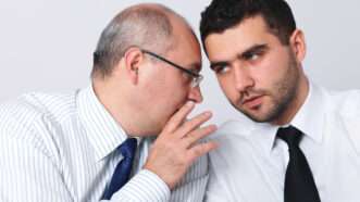 One businessman whispers to another, as if sharing a secret | Miszaqq | Dreamstime.com
