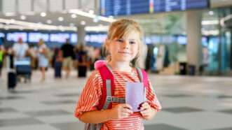 A young girl with a backpack and a passport in an airport terminal | Romrodinka | Dreamstime.com