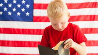 Boy reading the Bible in front of the American flag | Photo 85813446 © Vitaly Kraevski | Dreamstime.com