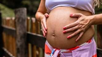 A pregnant woman holding her stomach | Photo by <a href=https://reason.com/category/health/medical-marijuana/