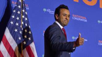 Vivek Ramaswamy gives a thumbs-up to attendees of NatCon 4 in Washington, D.C., in front of an orange and blue background and an American flag. | Dominic Gwinn/ZUMAPRESS/Newscom