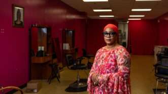 A woman stands in front of an empty hair salon, with her arms crossed and one hand over the other. | Photo: Institute for Justice