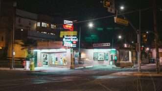 A street-corner liquor store lit up at night. | Photo by <a href=https://reason.com/category/culture/food/