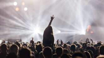 A woman in silhouette pumps her fist in the middle of the crowd at a rock concert, with stage lights blaring | Bjorn Hovdal | Dreamstime.com