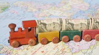 A toy train moves across a map of Asia, loaded with rolled-up U.S.  bills as its cargo. | Christopher Rawlins | Dreamstime.com