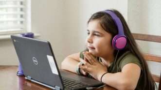 Girl wearing purple and pink headphones looking at a black laptop. | Photo by <a href="https://unsplash.com/@thomascpark?utm_content=creditCopyText&utm_medium=referral&utm_source=unsplash">Thomas Park</a> on <a href="https://unsplash.com/photos/a-little-girl-sitting-at-a-table-with-a-laptop-w9i7wMaM3EE?utm_content=creditCopyText&utm_medium=referral&utm_source=unsplash">Unsplash</a>