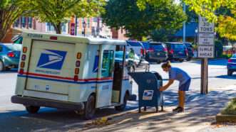 A USPS postal carrier collects mail from a mailbox on the sidewalk. | Georgesheldon | Dreamstime.com