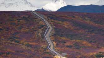 A pipeline goes up a hill, cutting through brush, with snowy mountains looming in the background. | DPST/Newscom