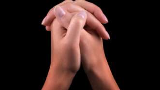 Two hands clasped in prayer, against a black background | Boule13 | Dreamstime.com