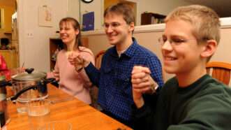 Uwe and Hannelore Romeike, with one of their children, holds hands at the dinner table. | Robin Nelson/ZUMA Press/Newscom