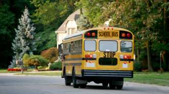 A yellow school bus drives through a residential neighborhood | Sonya Etchison | Dreamstime.com