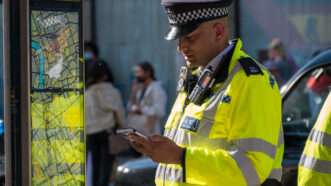 A British police officer in a neon vest looks at a cell phone. | Dave Cooil | Dreamstime.com