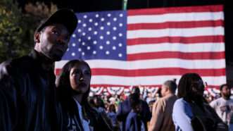 People stand in a crowd with a large American flag in the background | 	Jemal Countess/UPI/Newscom