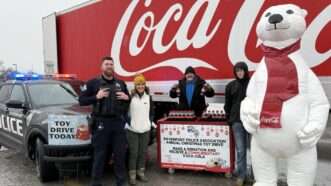 Coca-Cola truck and a Coca-Cola bear next to a Davenport Police Department squad car and officer and people behind a table running a charitable toy drive | Davenport Police Department/Facebook