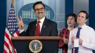 President Remy waves from behind the White House podium as his son an a reporter look on. | Reason TV