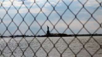 The Statue of Liberty as seen in the distance through a chain link fence. | Willeye | Dreamstime.com