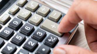 A hand presses the addition (+) button on a desk calculator. | Weerapat Wattanapichayakul | Dreamstime.com