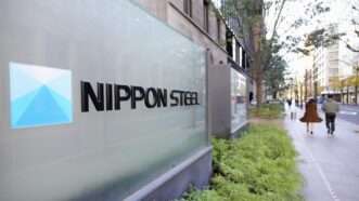 A sign for Nippon Steel sits next to a sidewalk that people are walking along | Kyodo/Newscom