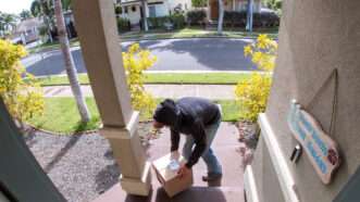 A "porch pirate," a man in a hoodie stealing a package off a front porch, as seen through a video doorbell. | RightFramePhotoVideo | Dreamstime.com