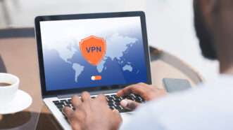 A black man uses a laptop, and on the screen is a VPN logo against a world map with an on/off toggle switch. | Prostockstudio | Dreamstime.com