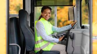 A woman in a reflective neon vest drives a school bus. | Prostockstudio | Dreamstime.com