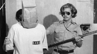 A man dressed as a prison guard corrals a man dressed as a prisoner with a bag over his head | <em>The Stanford Prison Experiment: Unlocking the Truth</em>/National Geographic