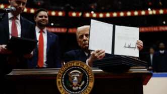 President Donald Trump holds up an executive order he just signed, on stage at Capital One Arena, seated behind a desk bearing the Presidential Seal. | Anna Moneymaker - Pool via CNP/Polaris/Newscom