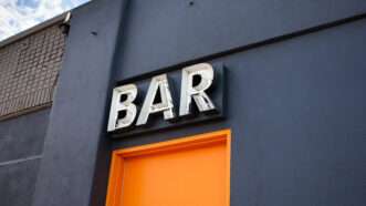 Dark building with an orange door, with a sign over it that says BAR. | David Tonelson | Dreamstime.com